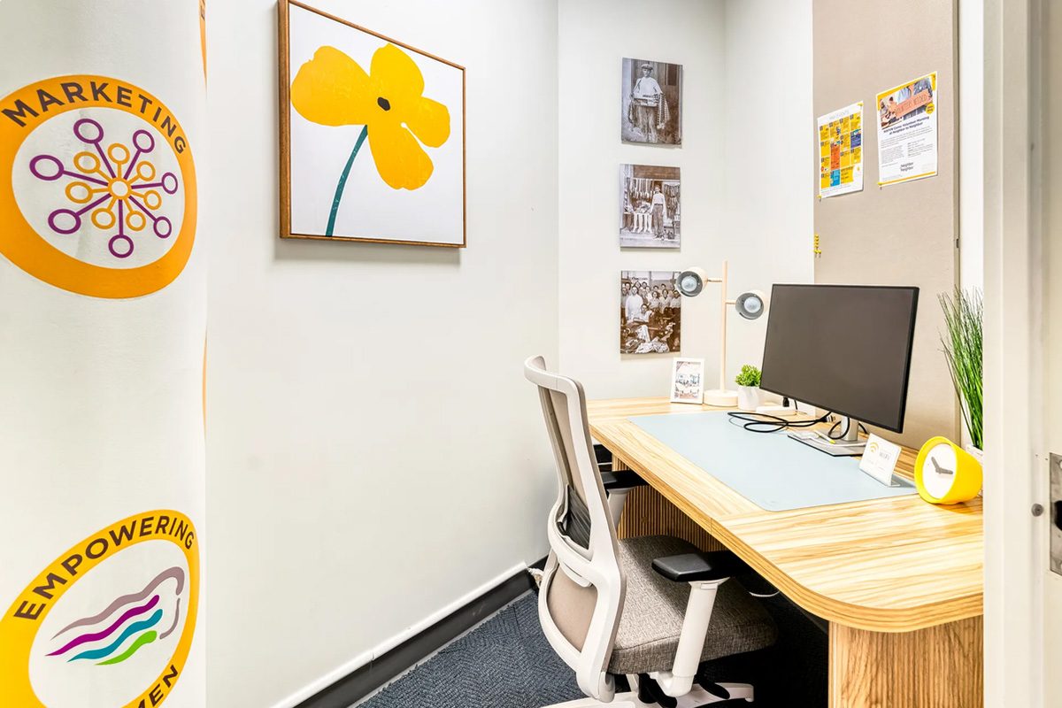 A HAYVN private office with a curved timber desk, monitor, task chair and a large yellow poppy painting on the wall