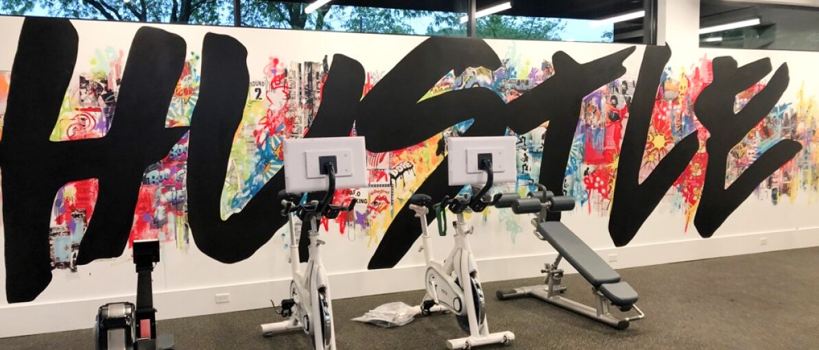 HAYVN's in-house fitness centre, with Peloton bikes in front of a wall-sized HUSTLE mural