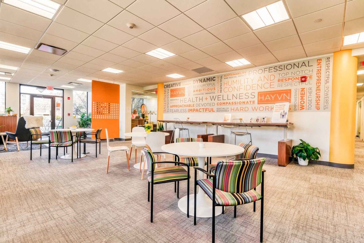 The open event space at HAYVN Greenwich, with striped armchairs, cafe tables and a full-height word wall reading HEALTH + WELLNESS